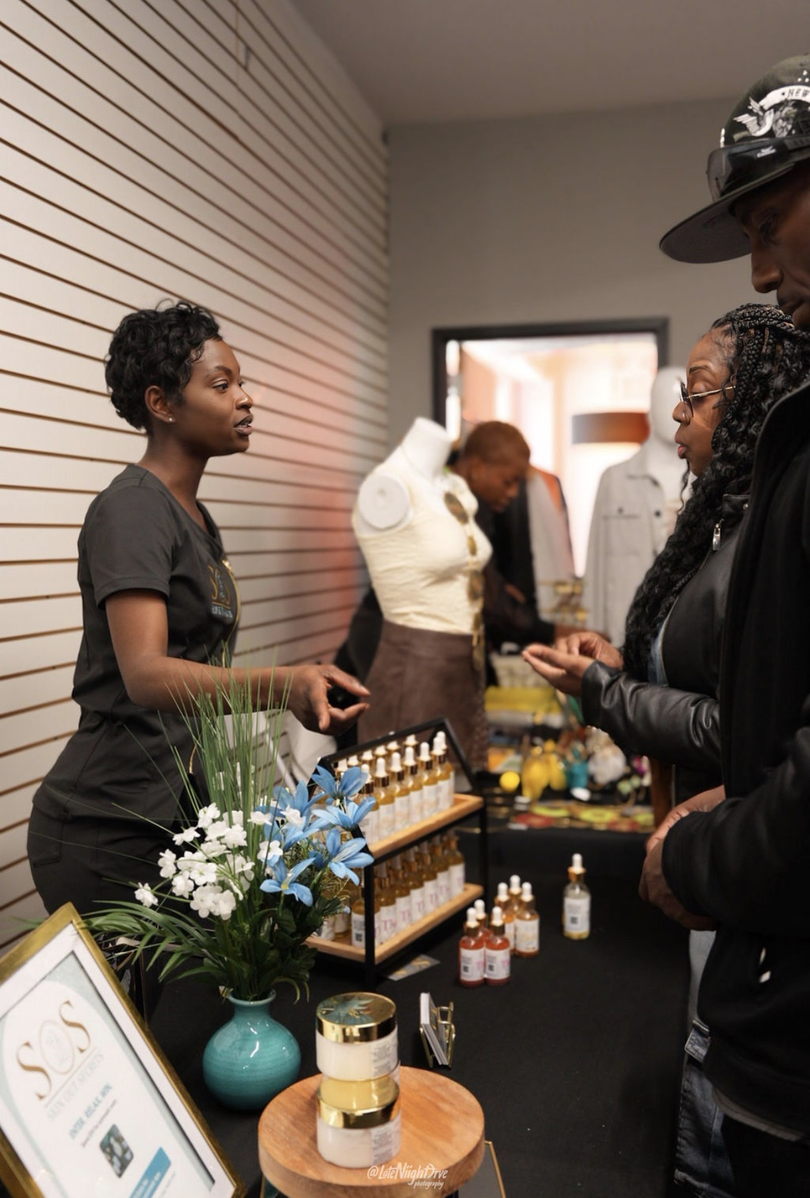 Founder of Skin Out Secrets talking with customers at a pop-up market table of body oils