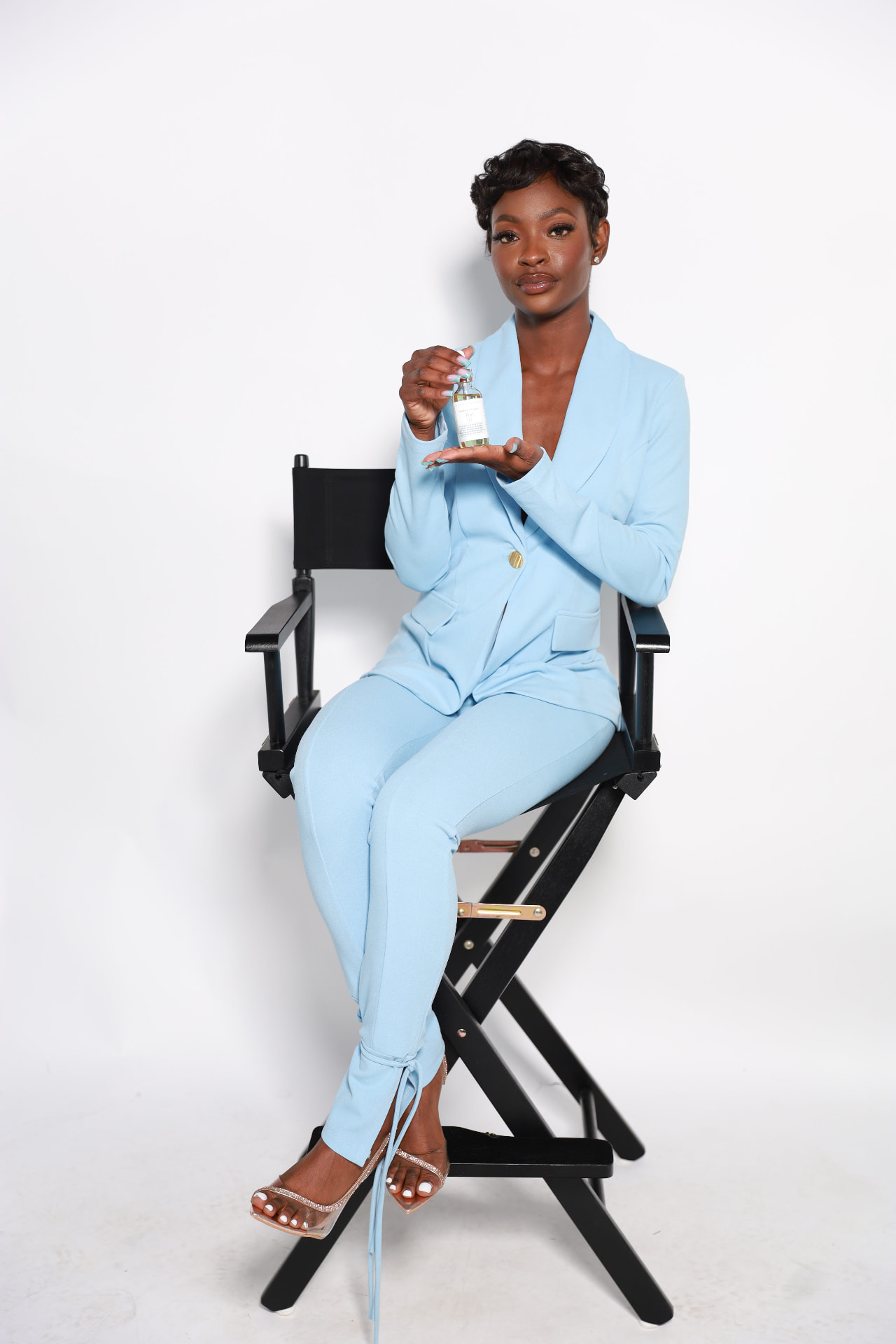Founder of Skin Out Secrets seated in a director's chair holding a bottle of body oil